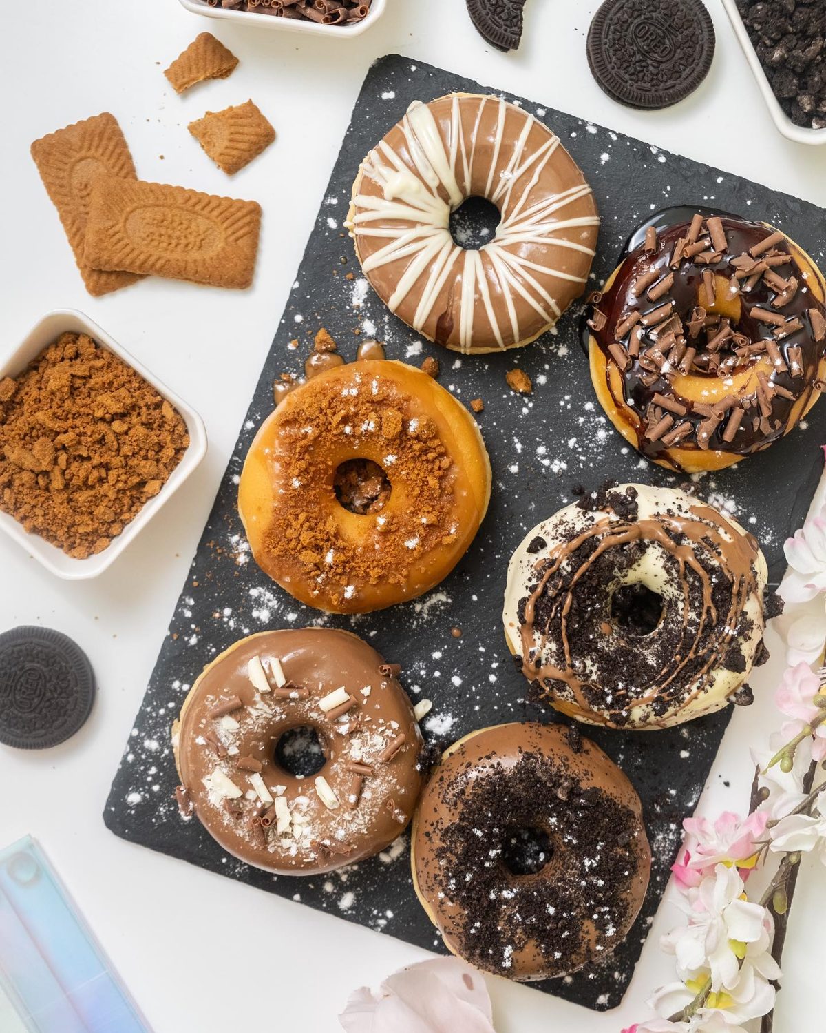 Six glazed doughnuts with Lotus, Oreo and chocolate toppings on a slate board