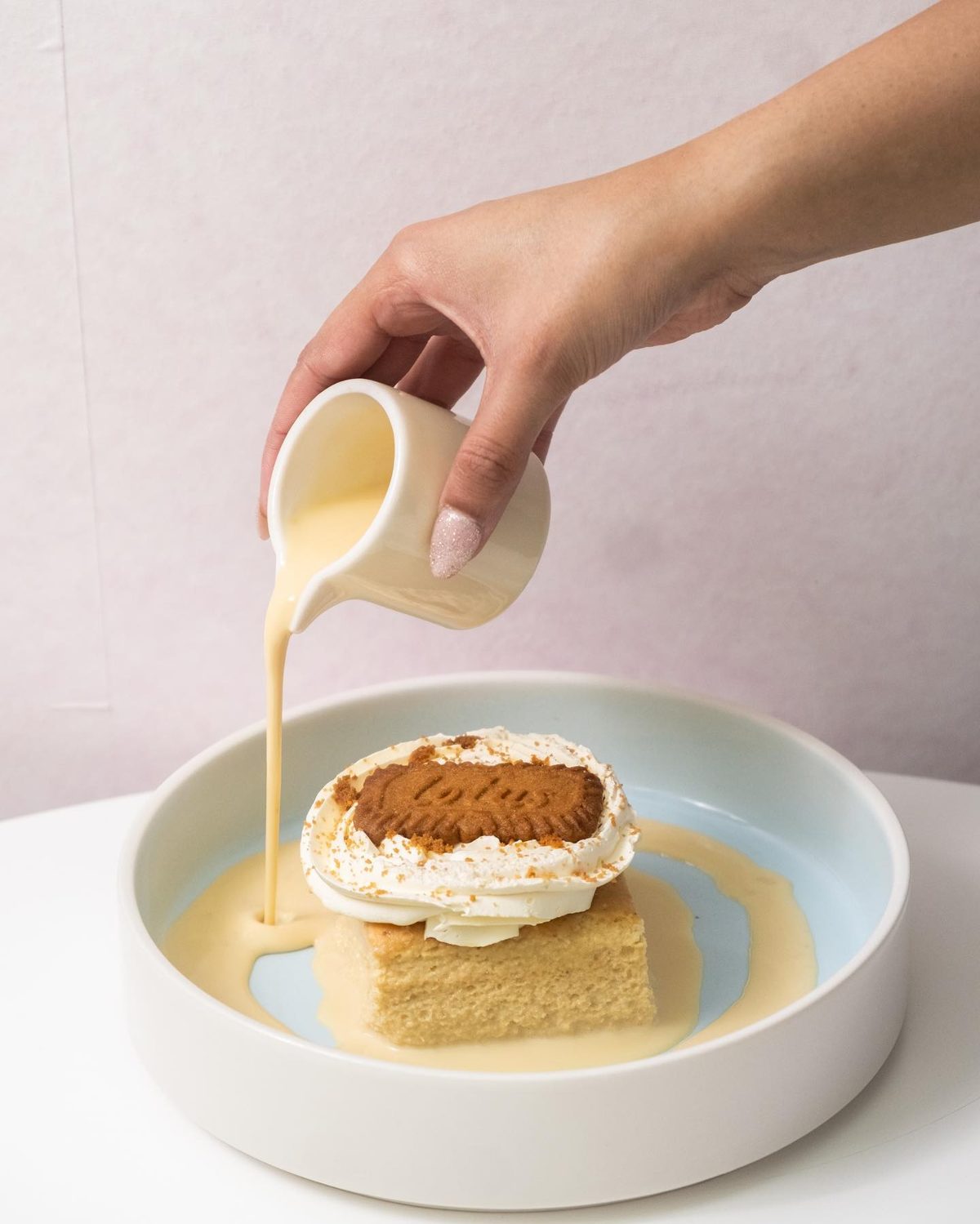 Cream being poured over a Lotus Biscoff tres leches cake topped with whipped cream